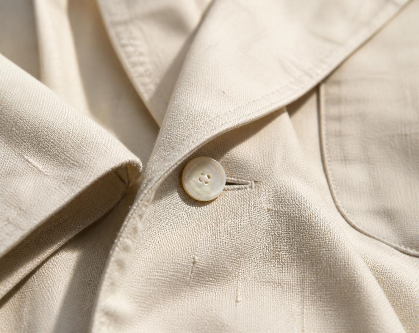 Macro detail of undyed cream linen suiting cloth, lapel roll and mother-of-pearl button
